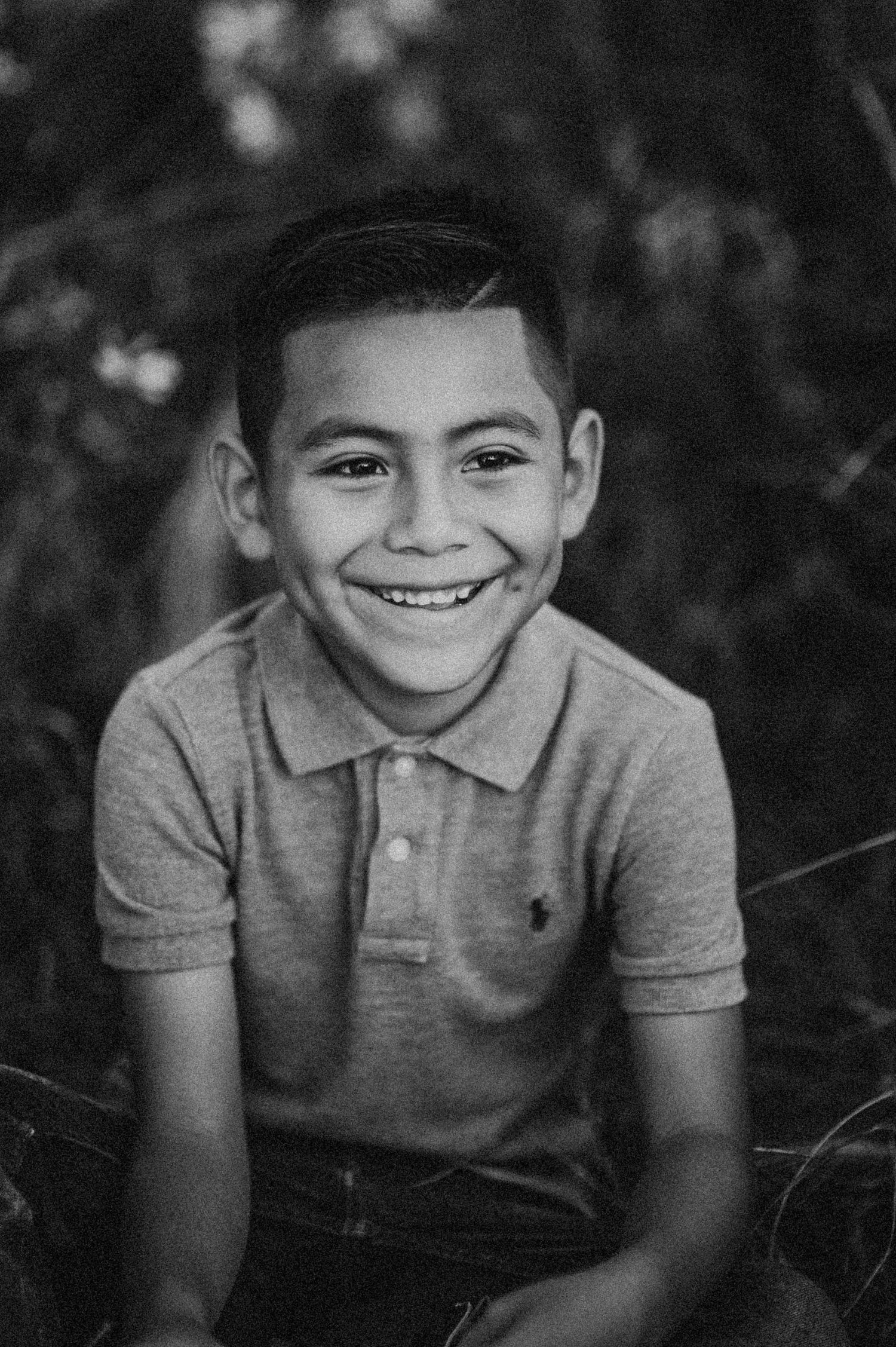 Smiling young boy in a polo shirt poses outdoors in a black and white portrait photo.