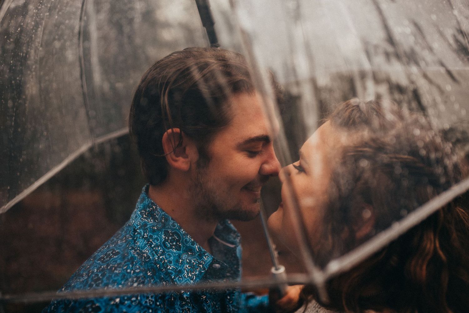Romantic couple sharing a kiss under a clear umbrella in the rain.