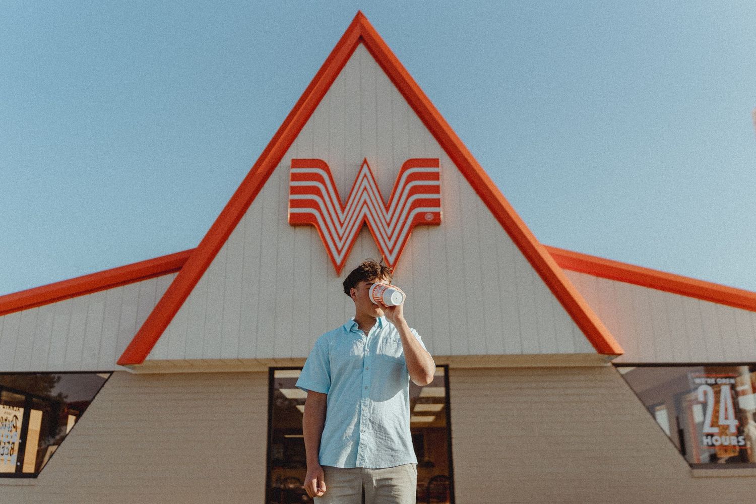 Man drinking a beverage outside a Whataburger restaurant with iconic red and white A-frame architecture.