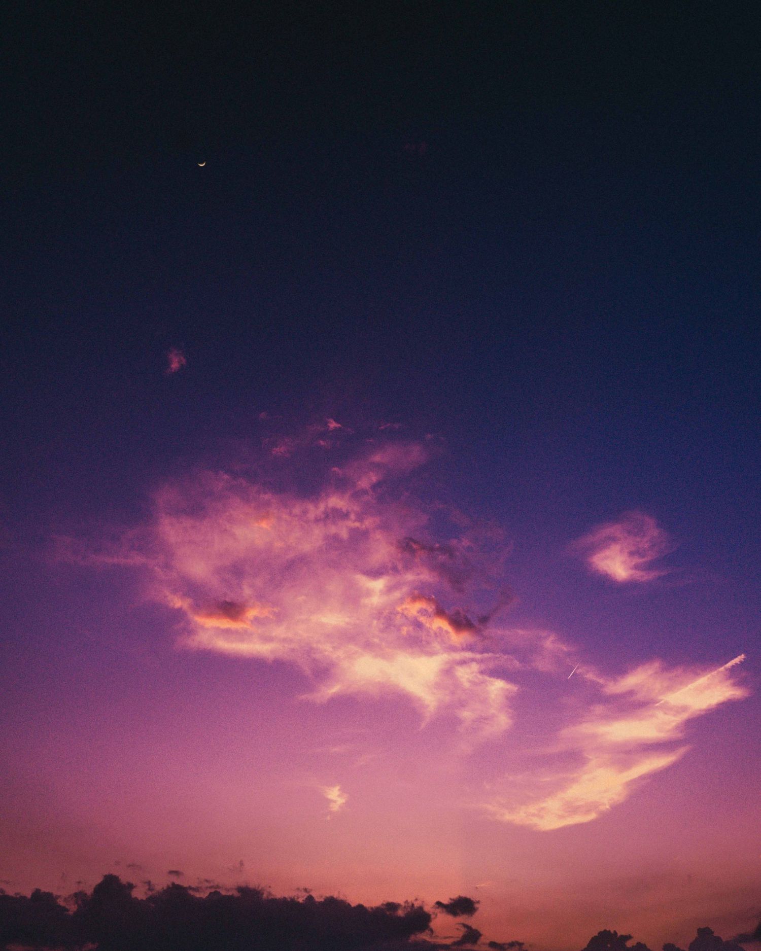 Vibrant purple and pink sunset sky with dramatic clouds and a crescent moon visible above the horizon.