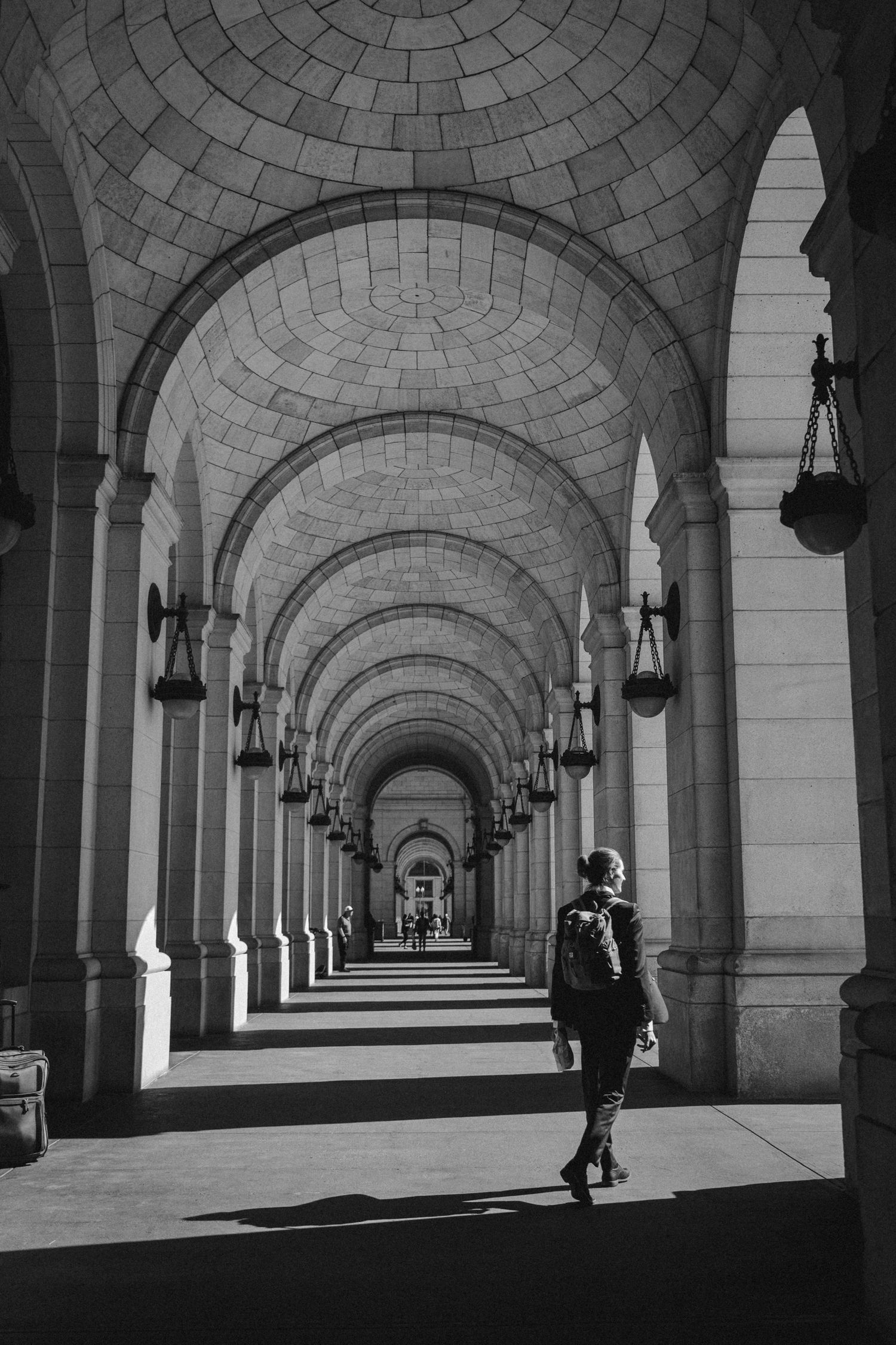 Black and white photo of a person walking through grand arched colonnade with dramatic perspective.
