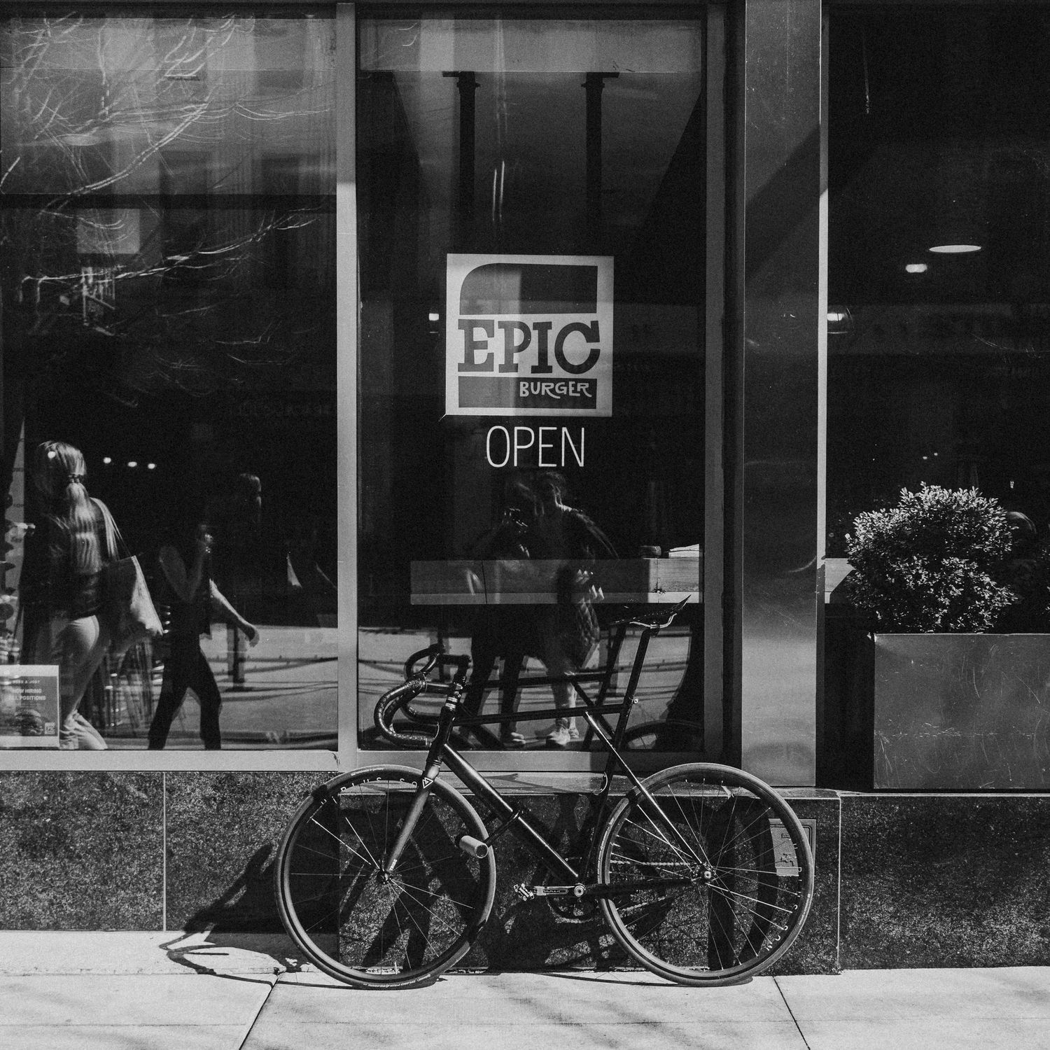 Black and white photo of a bicycle parked outside Epic Burger restaurant with an Open sign visible in the window.