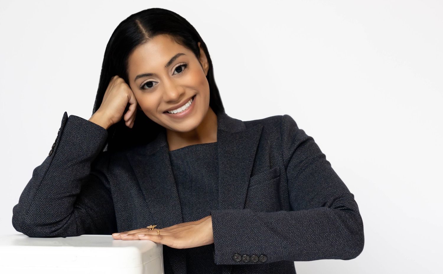 Smiling young businesswoman in gray blazer posing confidently against white background.
