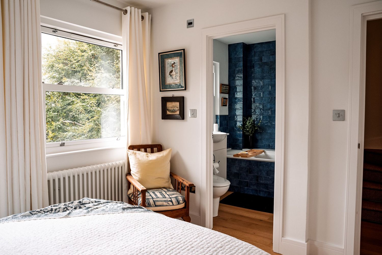 Bright bedroom with white walls, radiator, and en-suite bathroom featuring bold blue tiled walls.