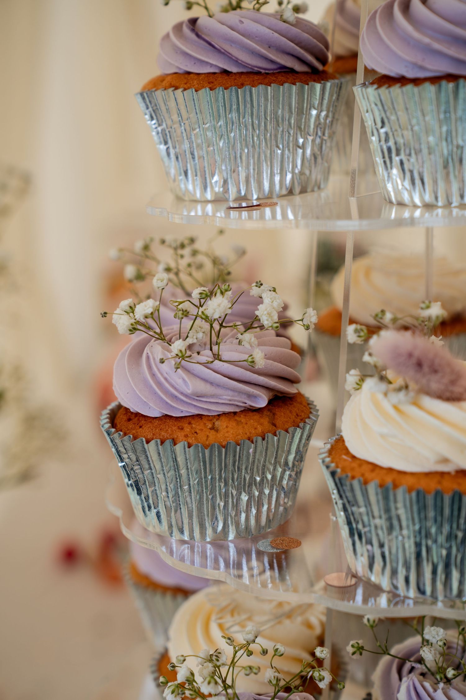 Elegant tiered display of purple frosted cupcakes in silver liners, decorated with delicate white flowers for a wedding.
