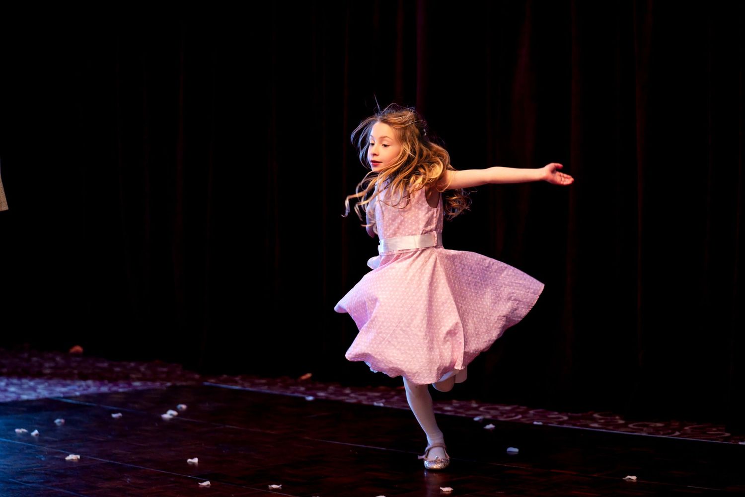 Young girl in pink tutu dress twirling gracefully on stage during a dance recital performance.