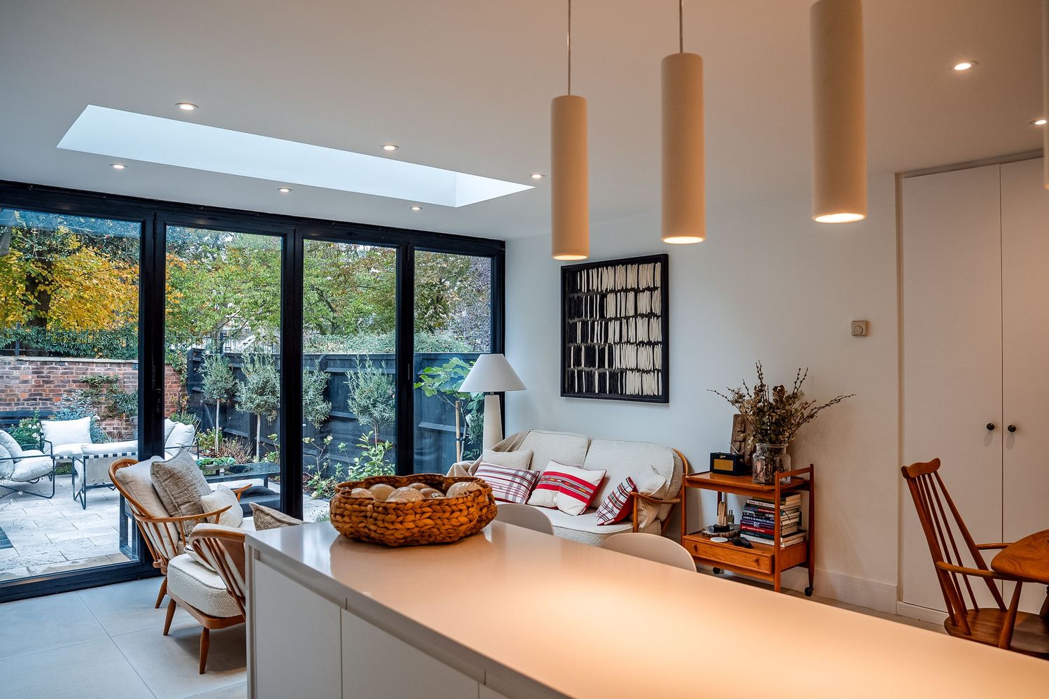 Modern open-plan living room with skylight, pendant lights, bi-fold garden doors, and stylish furniture in a bright white interior.