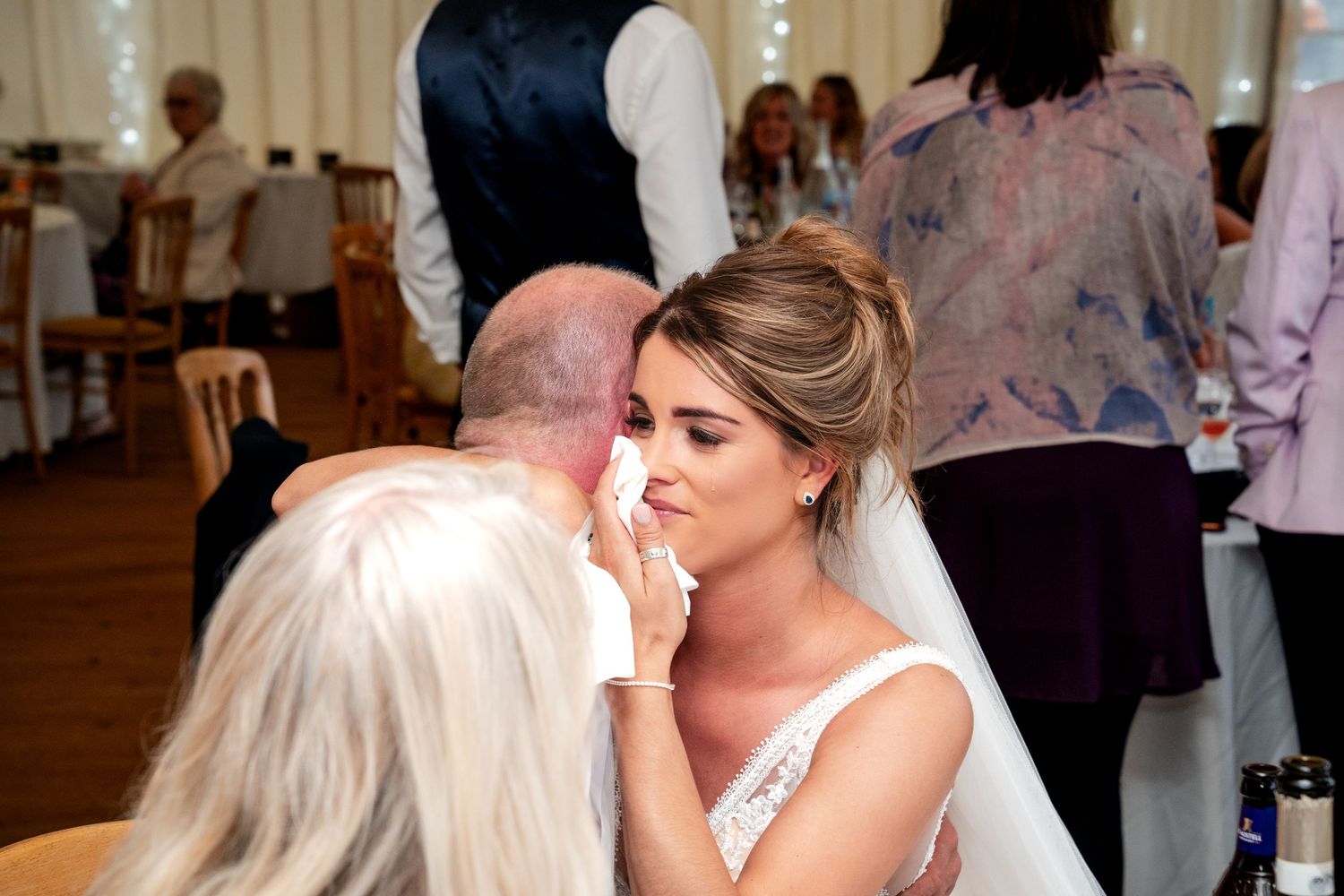 Emotional bride having makeup touched up by elderly woman at wedding reception in elegant venue.