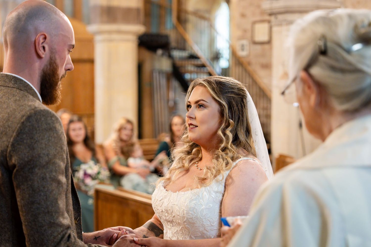 Bride in lace gown exchanges vows with groom at church altar during elegant wedding ceremony.