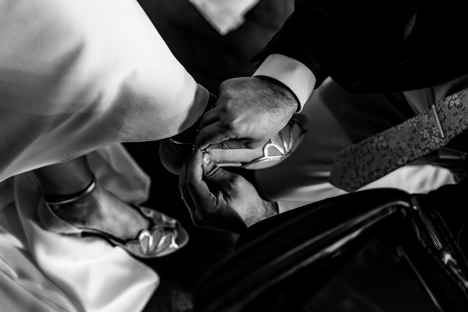 Black and white photo of hands fastening a cufflink, elegant wedding preparation detail shot.
