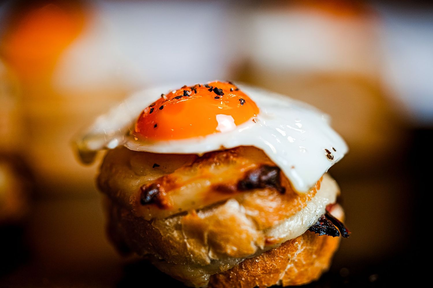 Close-up of a gourmet slider topped with a fried egg and black pepper on a toasted bun.