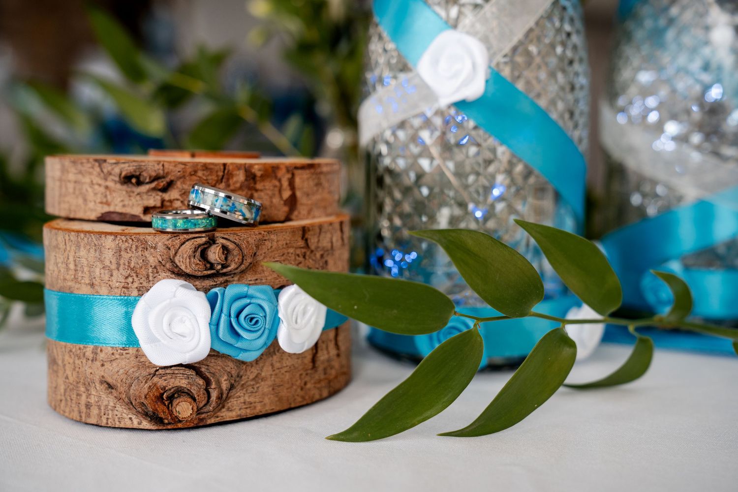 Rustic wooden slices with teal and white floral ribbons beside silver mercury glass vases at a wedding reception.