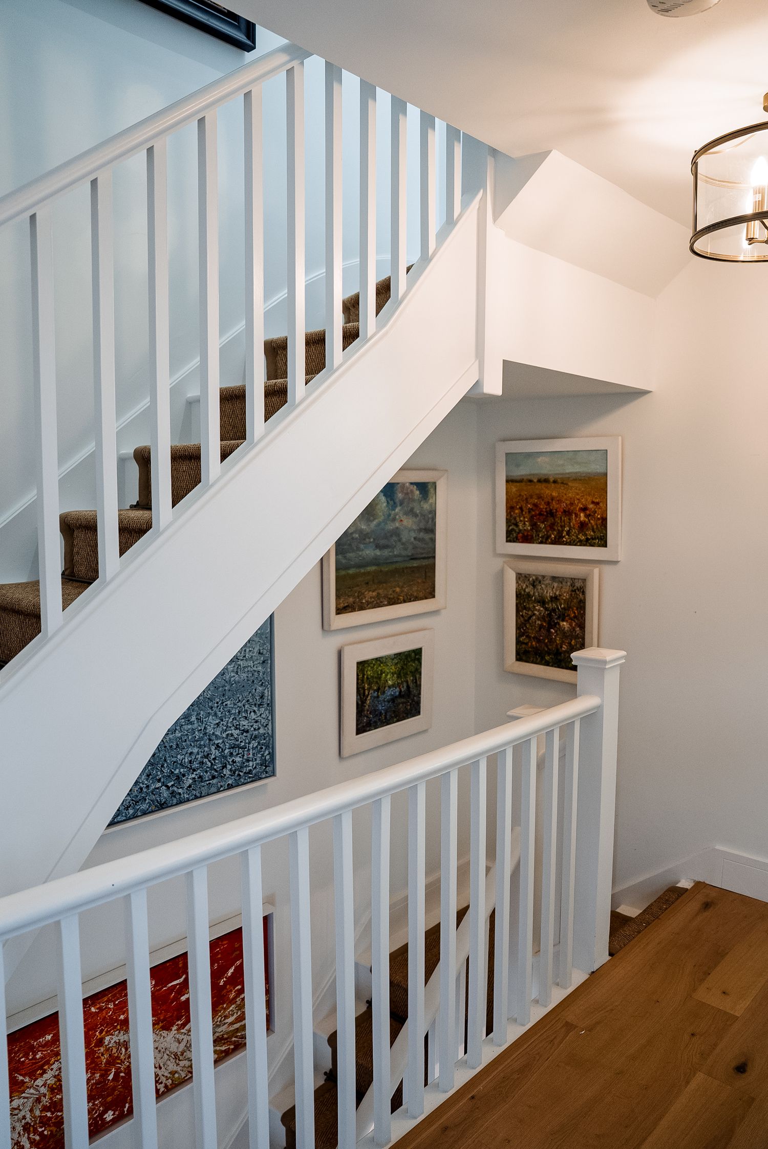 White staircase with carpet treads, framed landscape art on wall, and hardwood floors in a bright home interior.