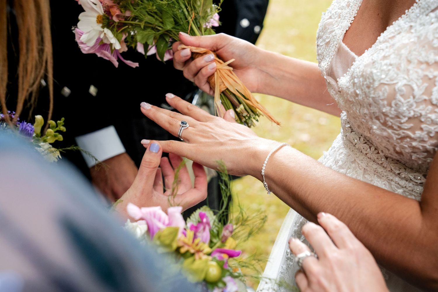 Close-up of bride and groom exchanging wedding rings during outdoor ceremony, bride holding colorful flower bouquet.