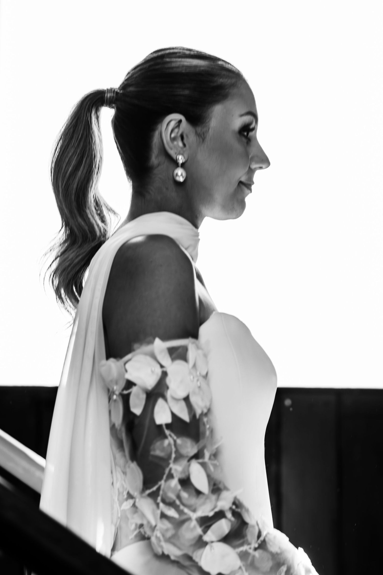 Black and white profile portrait of a bride in floral dress with ponytail and drop earrings.
