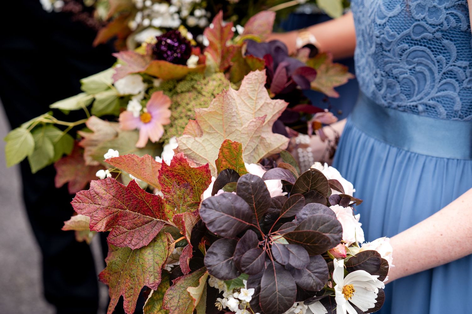 Autumn wedding bouquet with colorful fall leaves held by bridesmaid in blue lace dress.