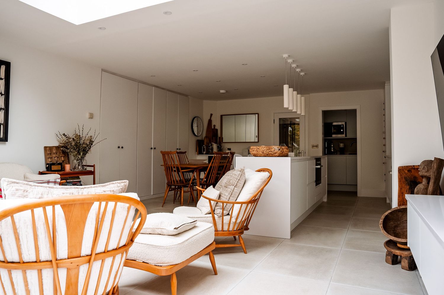 Modern open-plan living room with rattan chairs, white cushions, and a sleek kitchen in the background.