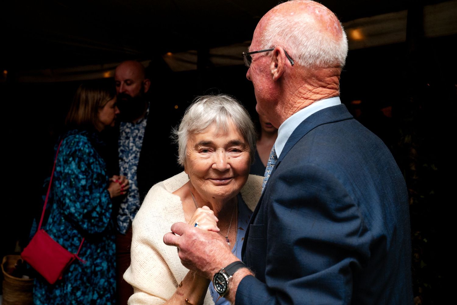 Elderly couple sharing a warm embrace at an indoor social gathering event.