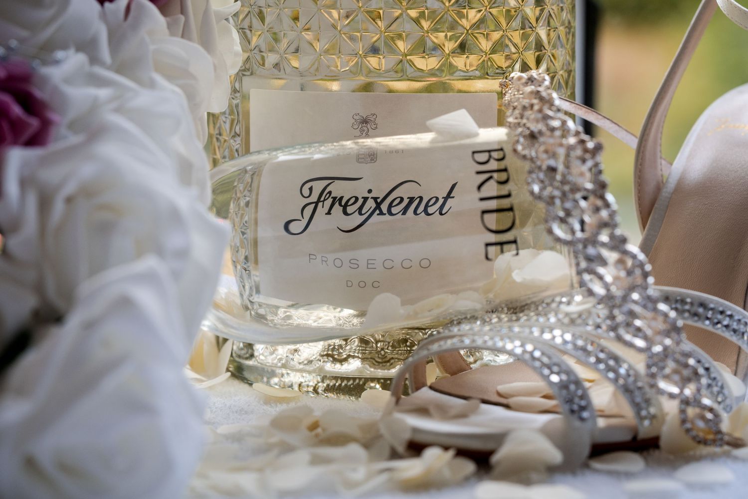 Freixenet Prosecco bottle with a sparkling rhinestone Bride tiara and white flower petals at a wedding celebration.