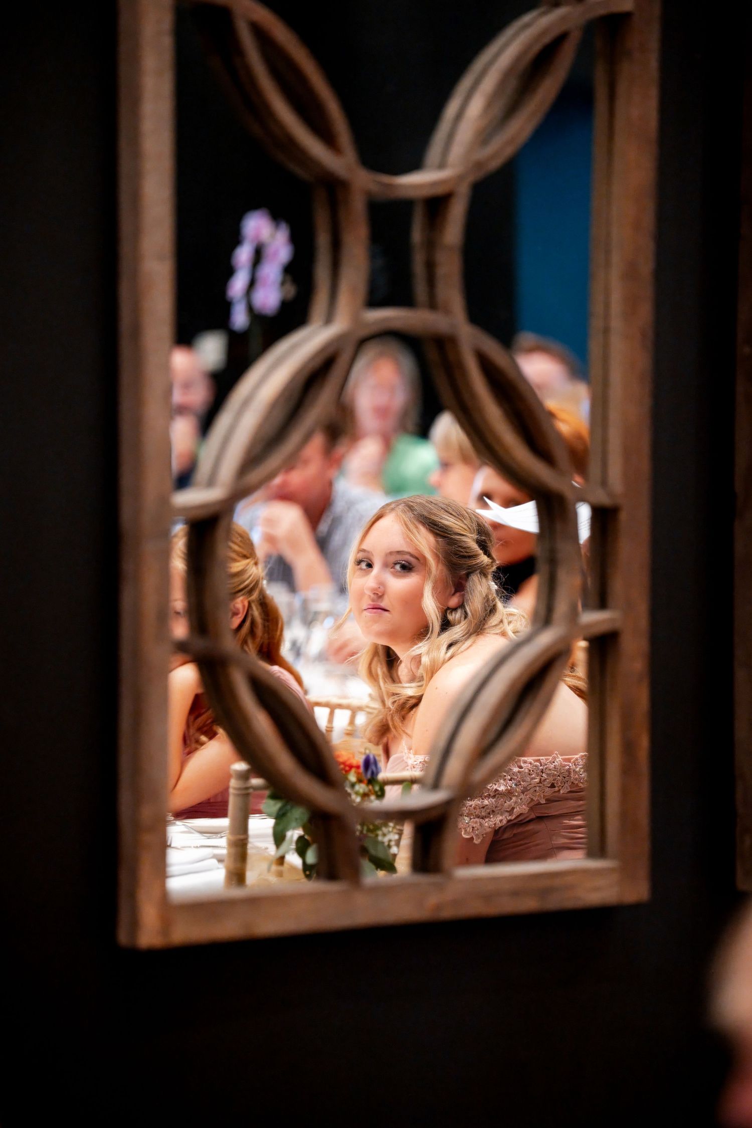 Young woman at a wedding reception viewed through decorative wooden lattice frame at an elegant event.