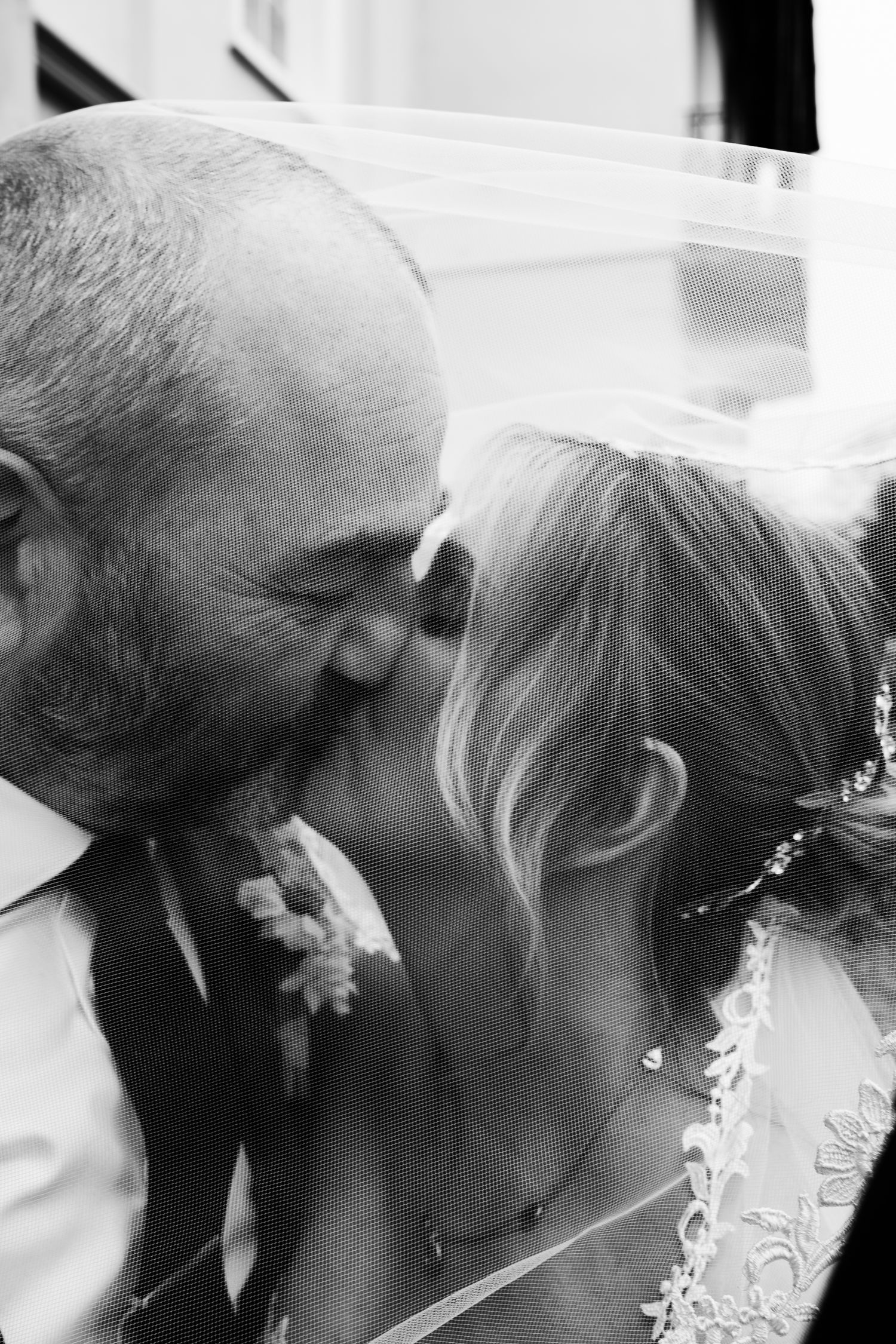 Black and white photo of a bride and groom sharing a tender kiss under a veil on their wedding day.