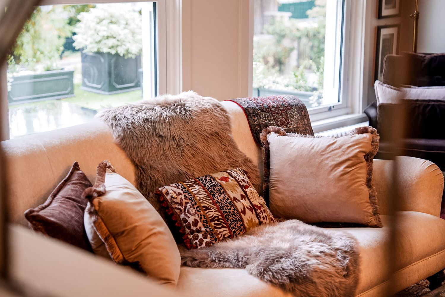 Cozy beige sofa adorned with mixed fur, animal print, and velvet throw pillows near a sunlit window.