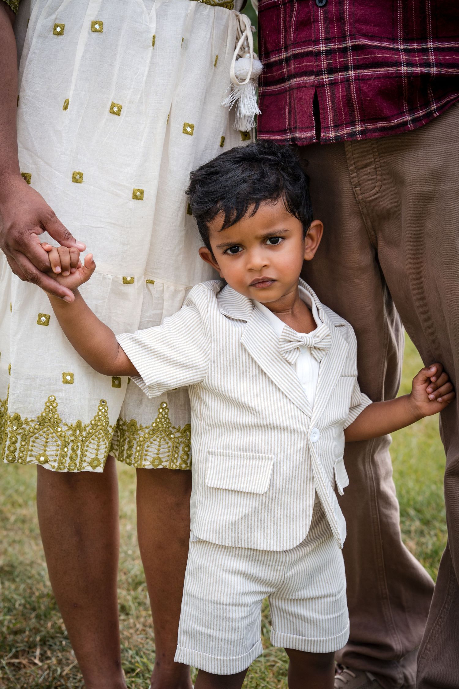 Young boy in white suit holding hands with parents outdoors.