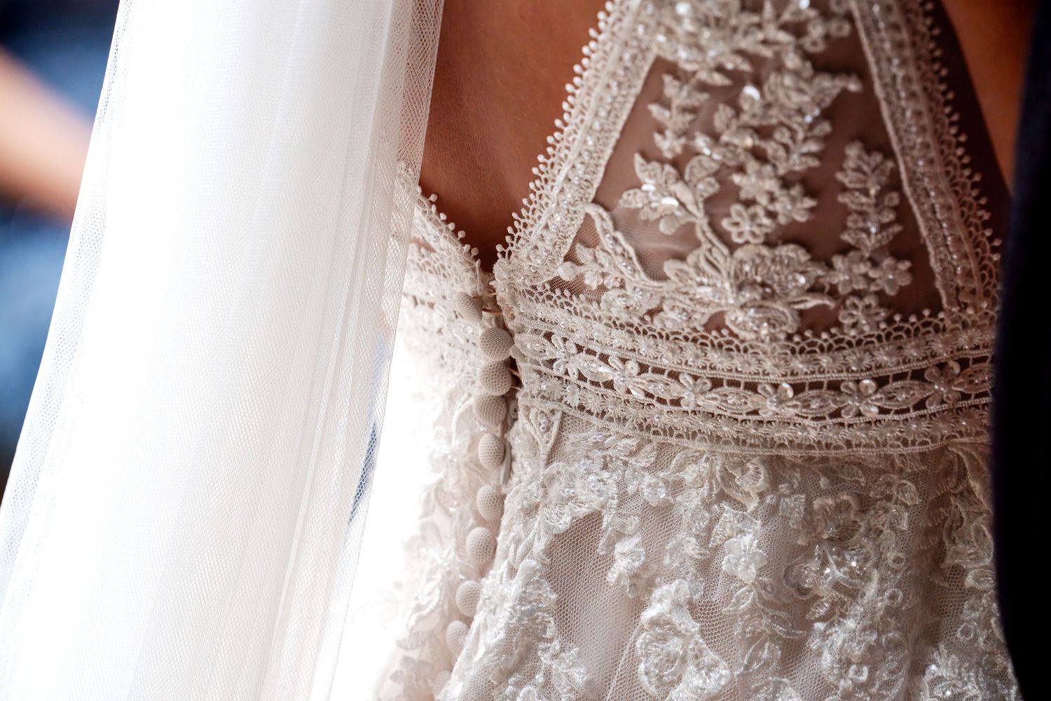 Close-up of an intricate lace wedding dress with floral embroidery and sheer back detail, adorned with a flowing bridal veil.