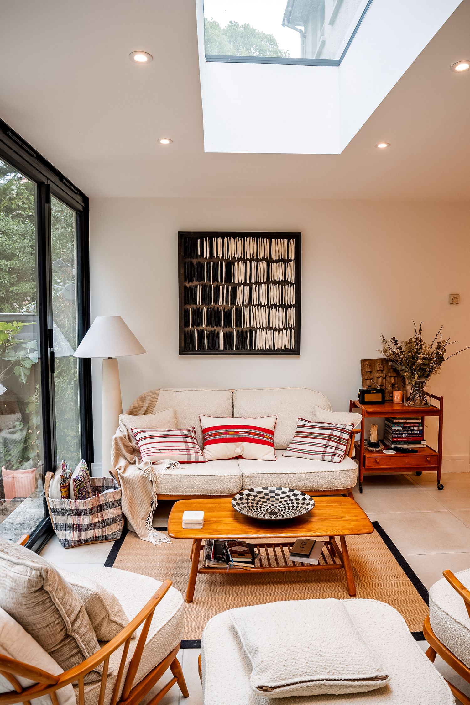 Bright modern living room with skylight, cream sofa, red accent pillows, wood coffee table, and large abstract wall art.