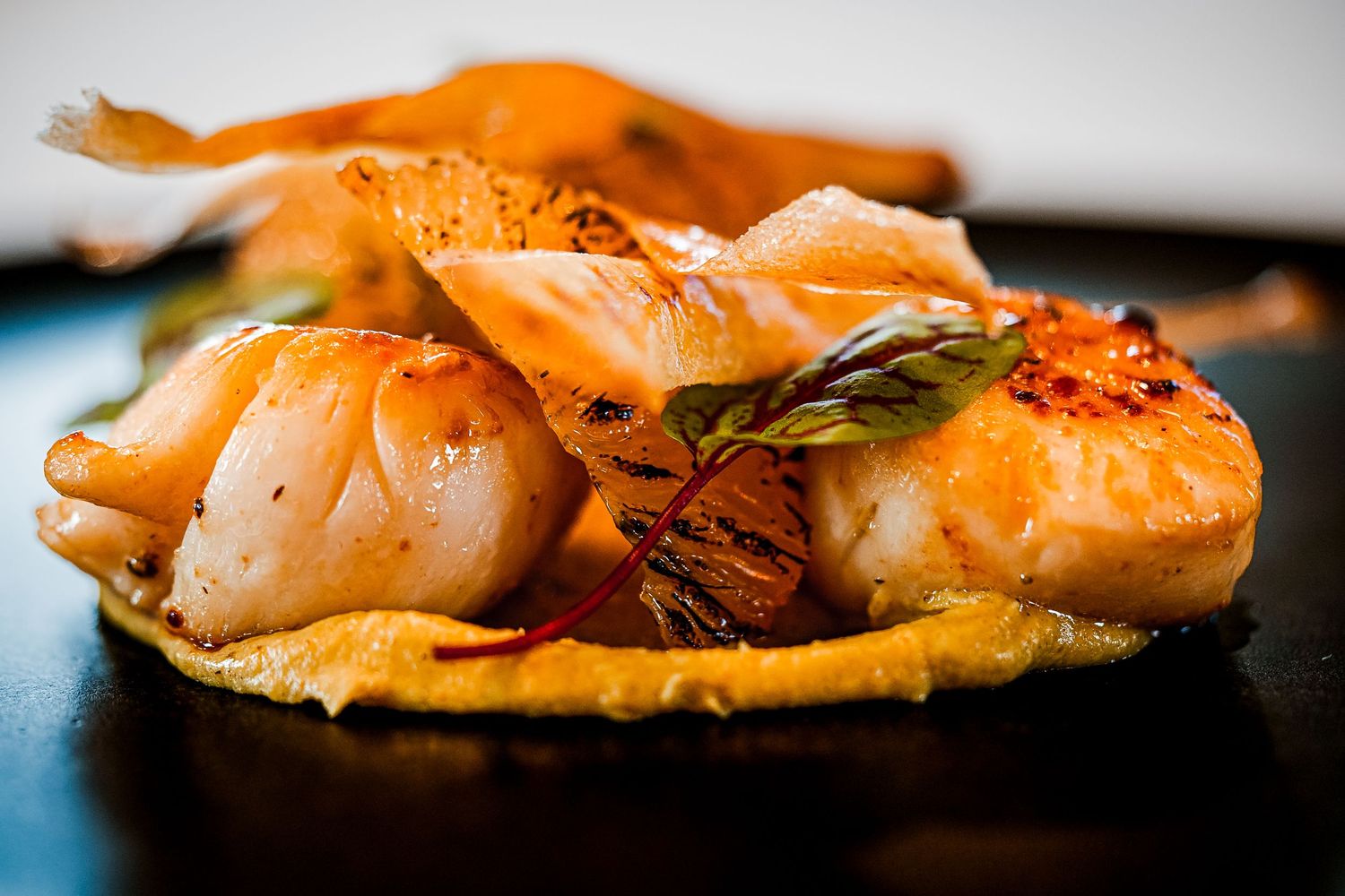 Gourmet seared shrimp with golden crispy base, garnished with fresh herbs and chili flakes on a dark plate.