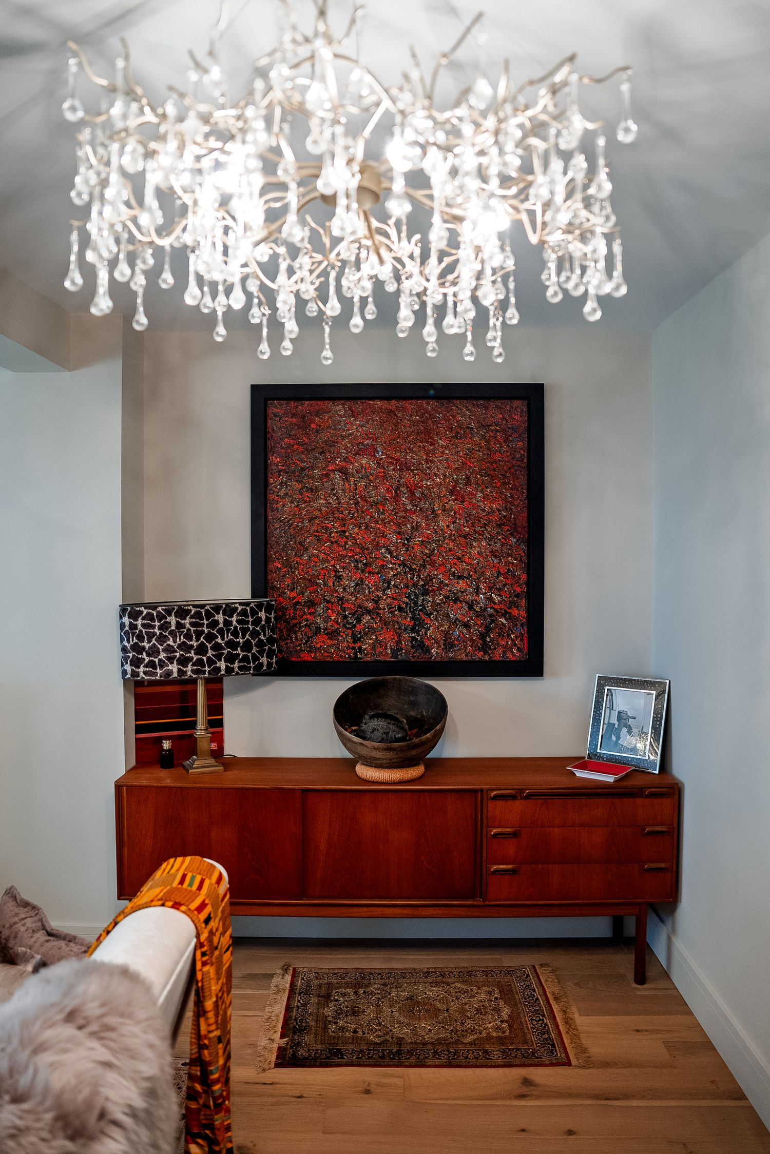 Mid-century modern credenza with red abstract painting, crystal chandelier, patterned rug, and decorative bowl in stylish interior.