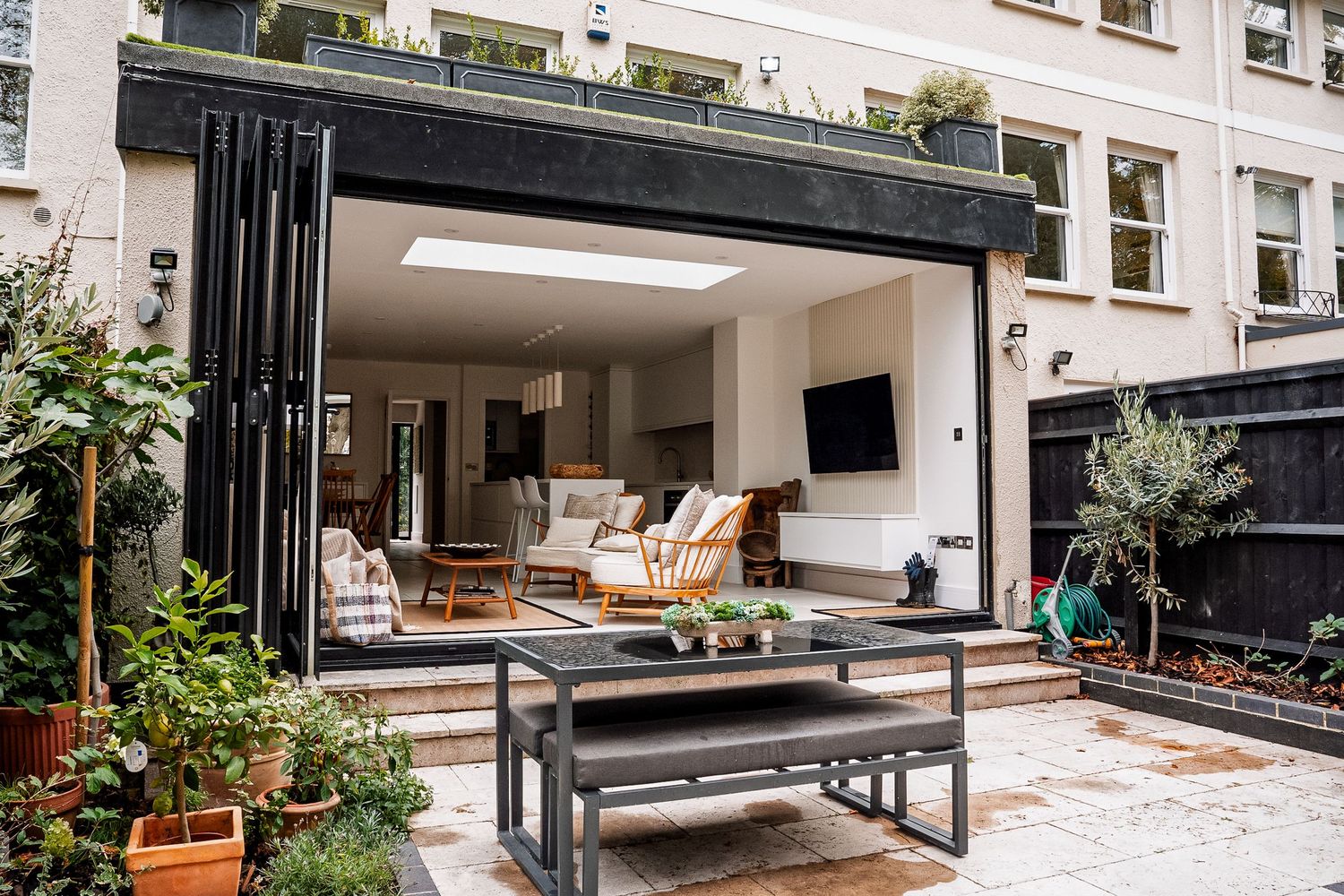 Modern home with open bifold doors connecting indoor living space to a patio garden with outdoor dining table.