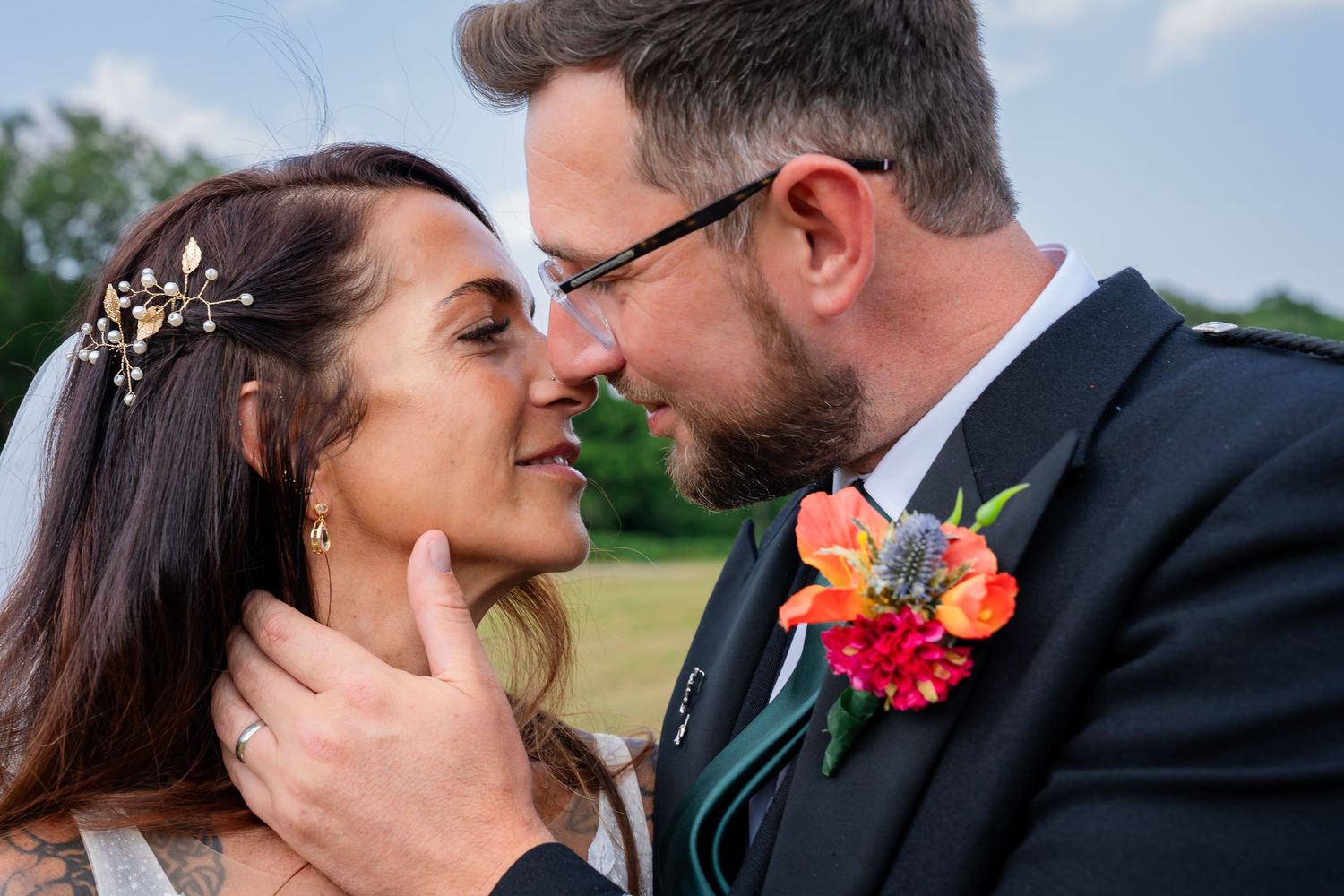 A bride and groom share an intimate moment, nearly kissing outdoors, with colorful boutonniere and bridal hair accessories.