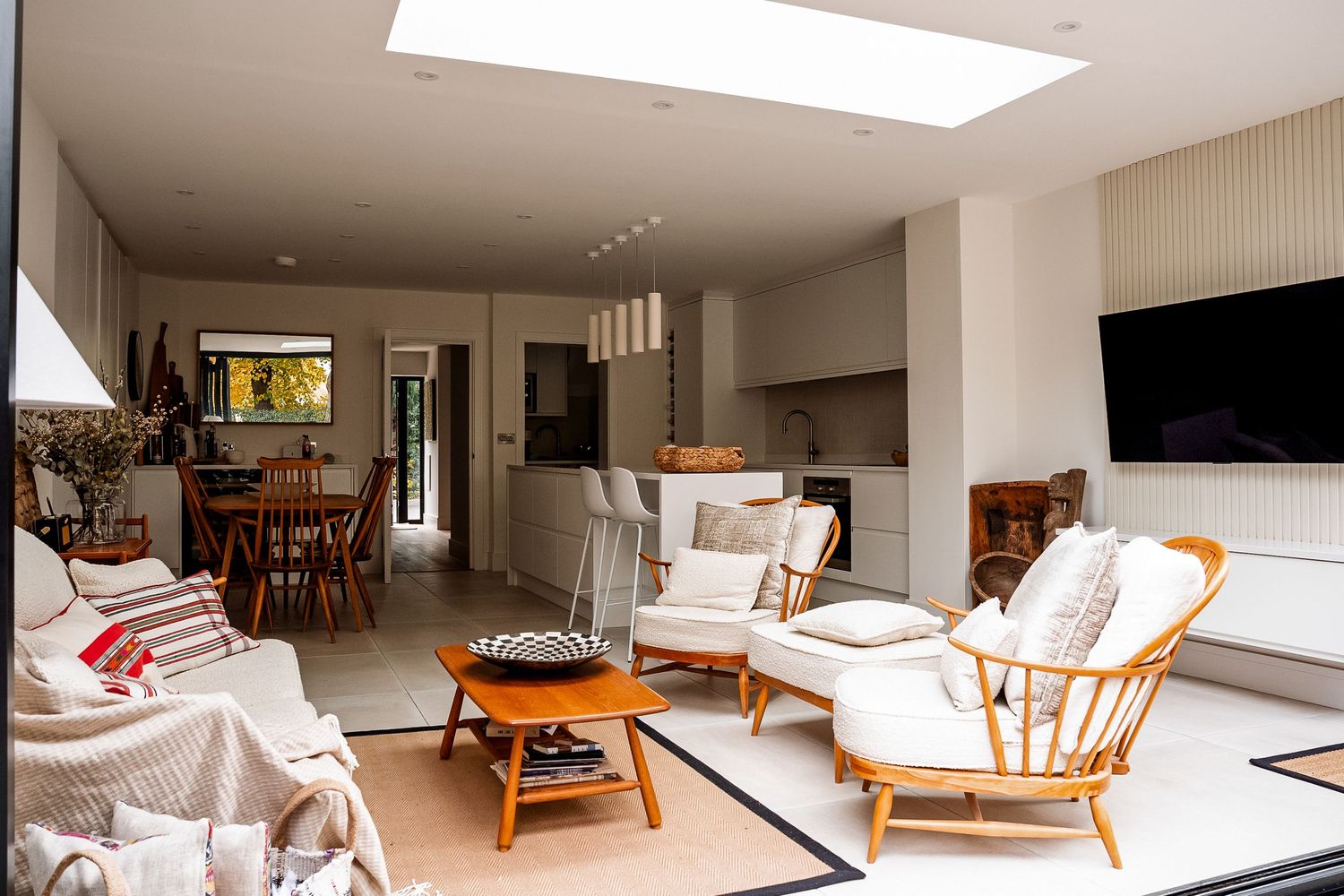 Bright open-plan living room with rattan chairs, white sofas, skylight, and open kitchen dining area in modern home.