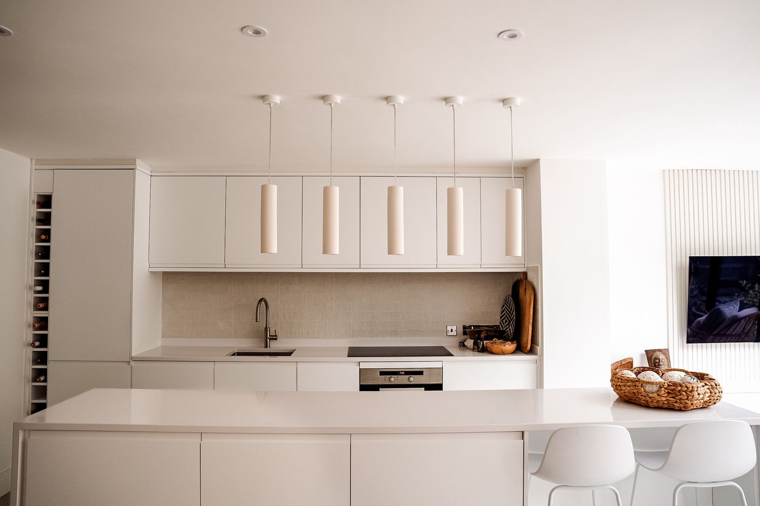 Modern minimalist white kitchen with pendant lights, sleek cabinetry, island seating, and a clean neutral aesthetic.