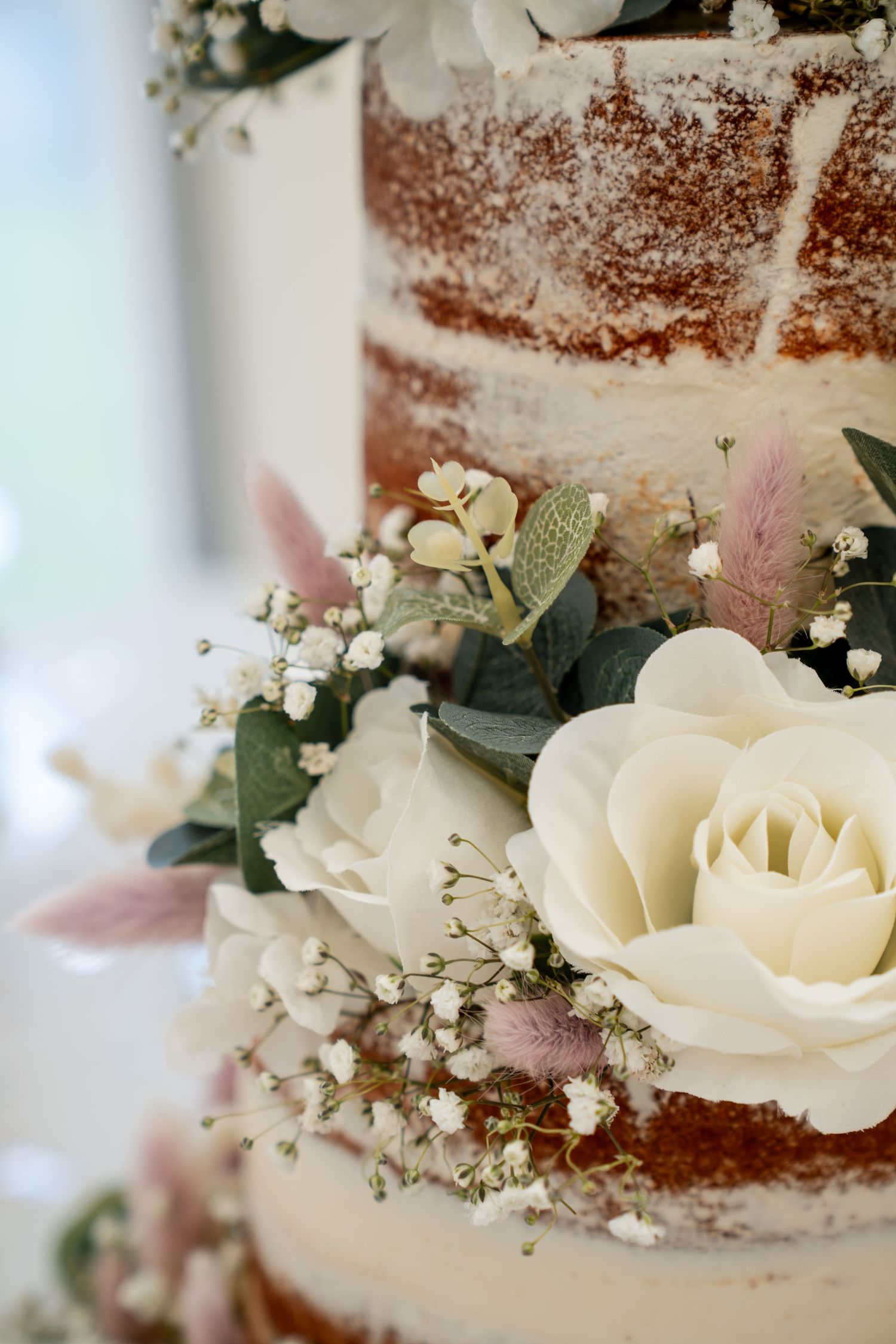 Elegant semi-naked wedding cake adorned with white roses, baby's breath, and eucalyptus leaves between red velvet layers.