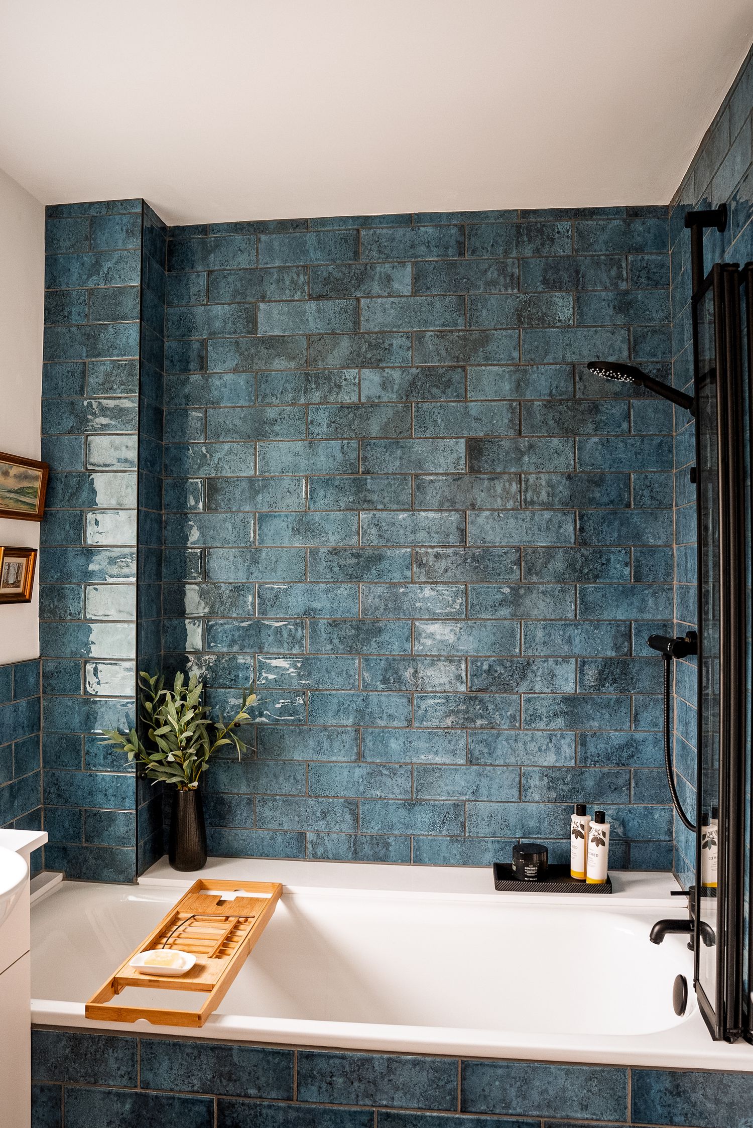 Luxurious bathroom with teal zellige tiles, white soaking tub, bamboo bath caddy, and black shower fixtures.