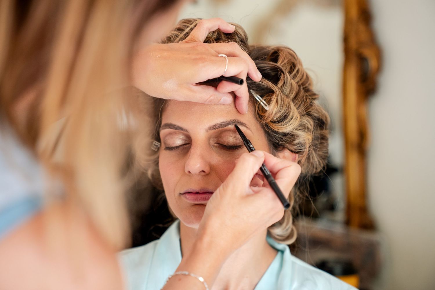A makeup artist applying eyeliner to a woman with an updo hairstyle, preparing her for a special occasion.