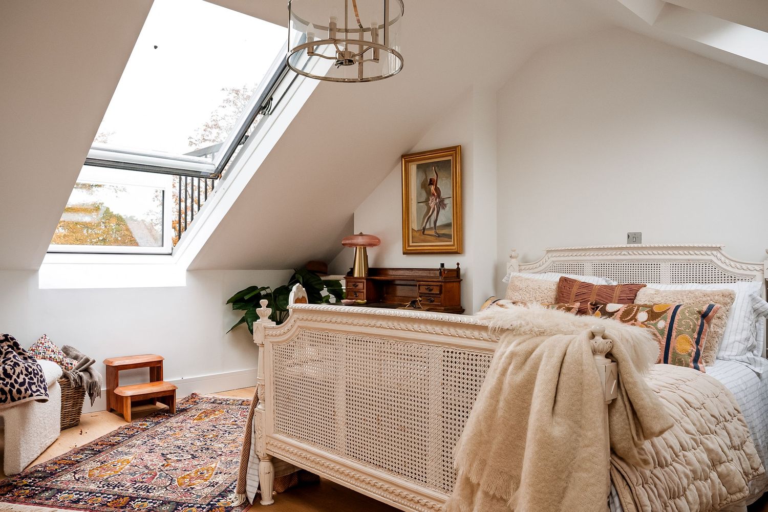 Cozy attic bedroom with wicker bed frame, skylight window, patterned rug, and bohemian decor in white room.
