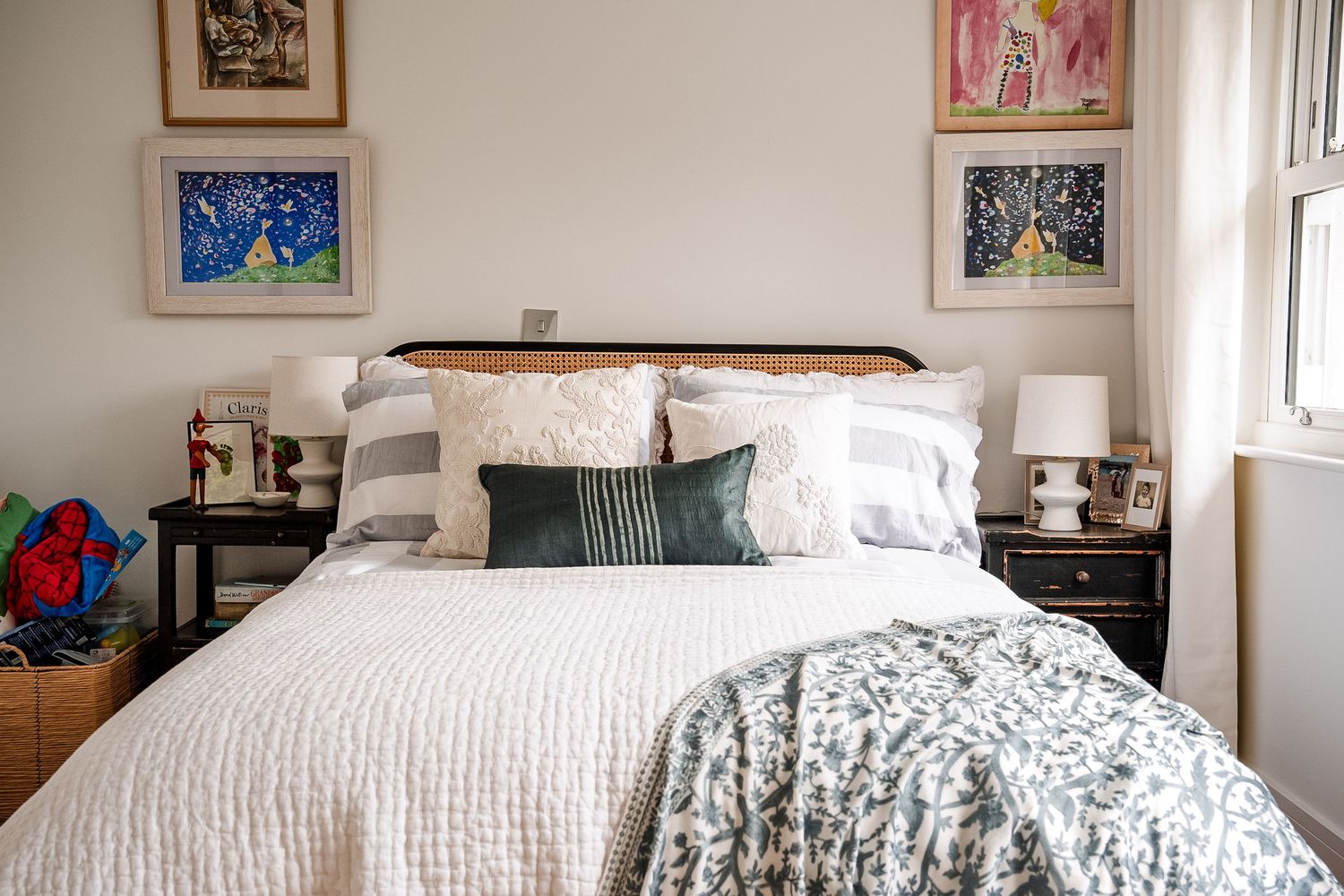 Cozy bedroom with white bedding, green accent pillows, dark wood nightstands, and colorful framed artwork above the headboard.