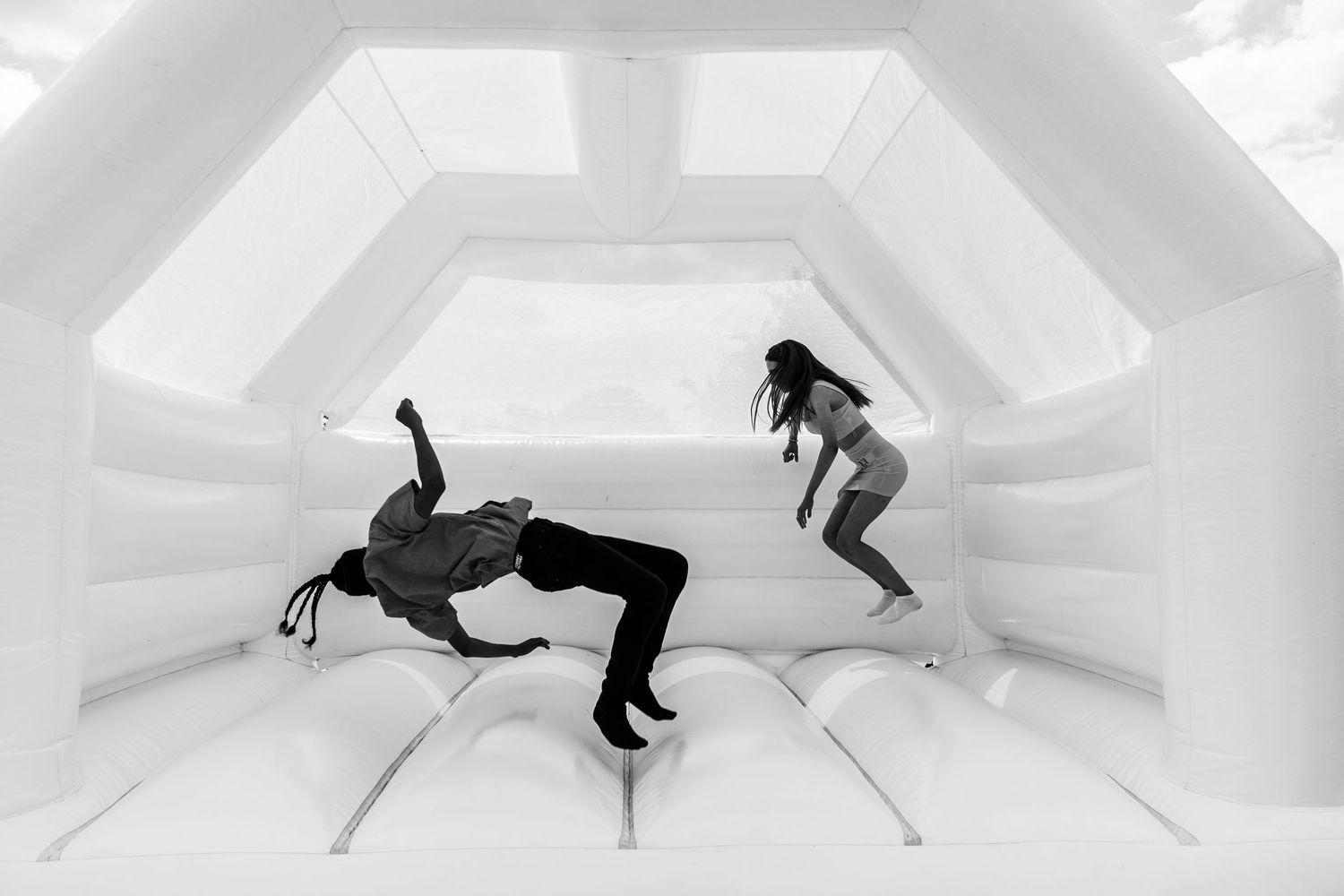 Two people jumping and playing in a white inflatable bounce house, captured in black and white photography.
