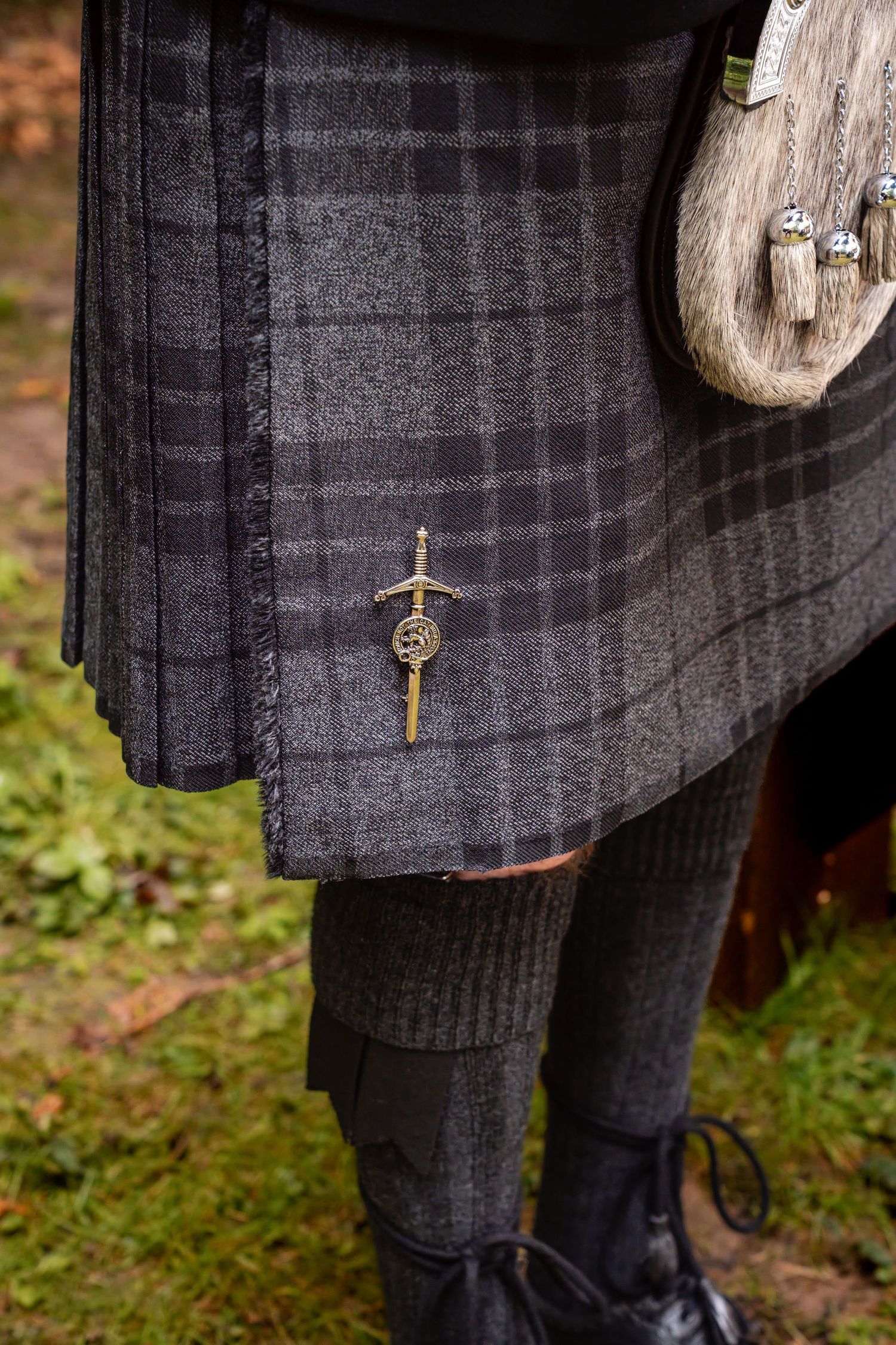 Close-up of a traditional Scottish kilt in gray tartan with a decorative sgian-dubh pin and sporran.