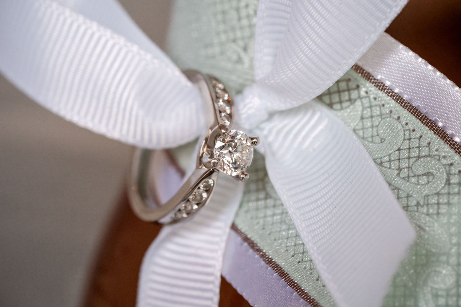 Diamond engagement ring with silver band resting on white and mint green ribbon bow.