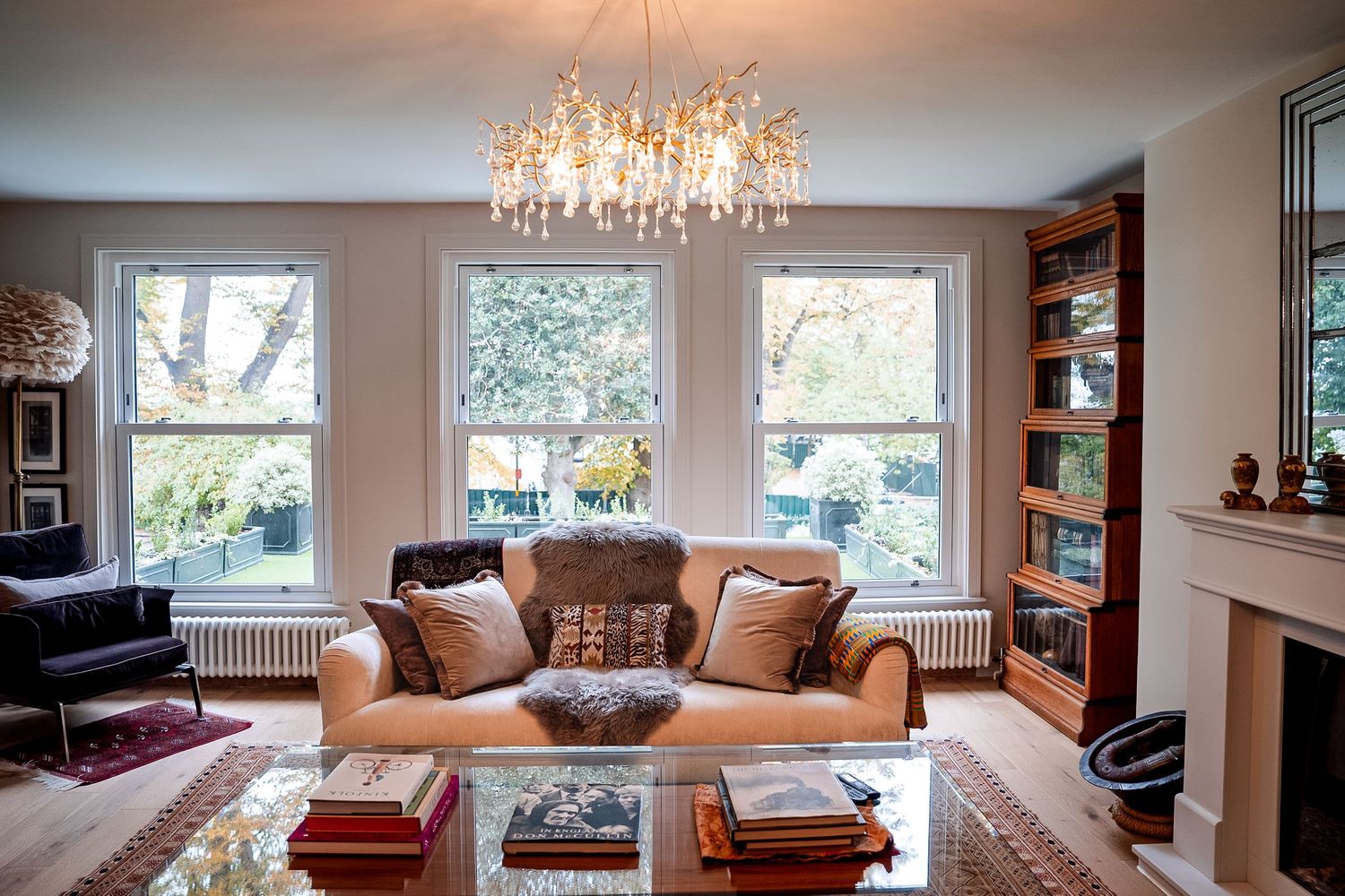 Elegant living room with cream sofa, ornate chandelier, built-in bookcase, and large windows overlooking a garden.