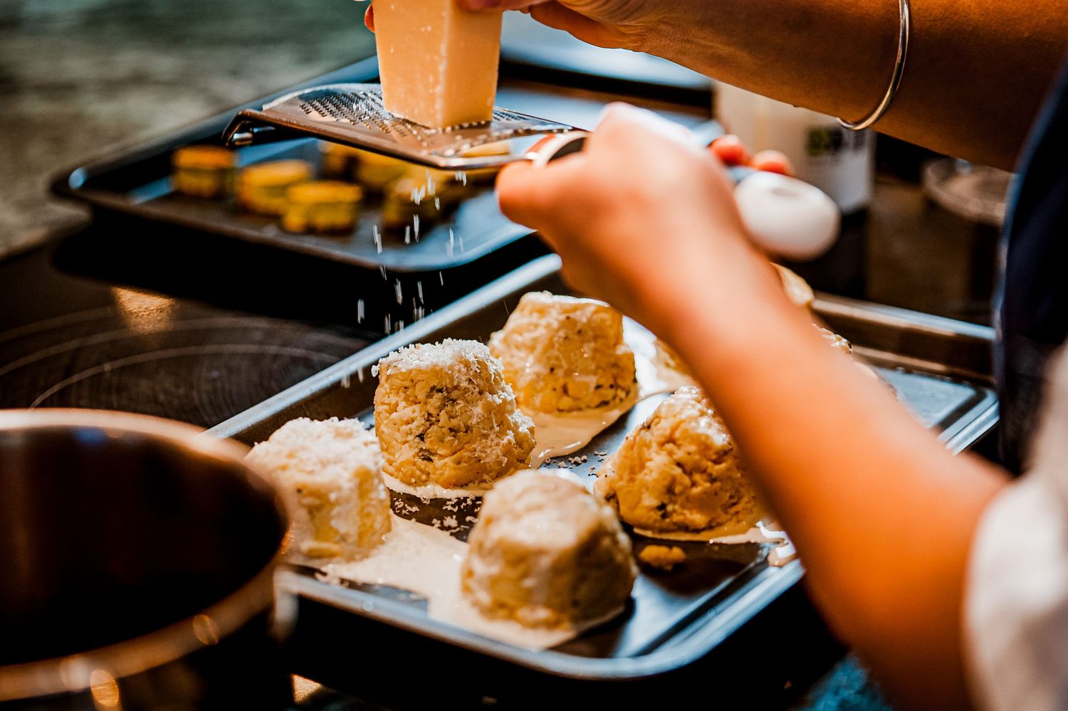 Person dusting powdered sugar over freshly baked scones on a dark baking tray lined with parchment paper.
