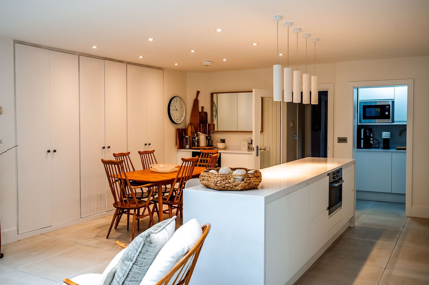Modern open-plan kitchen and dining area with white cabinetry, pendant lights, island counter, and wooden dining table.