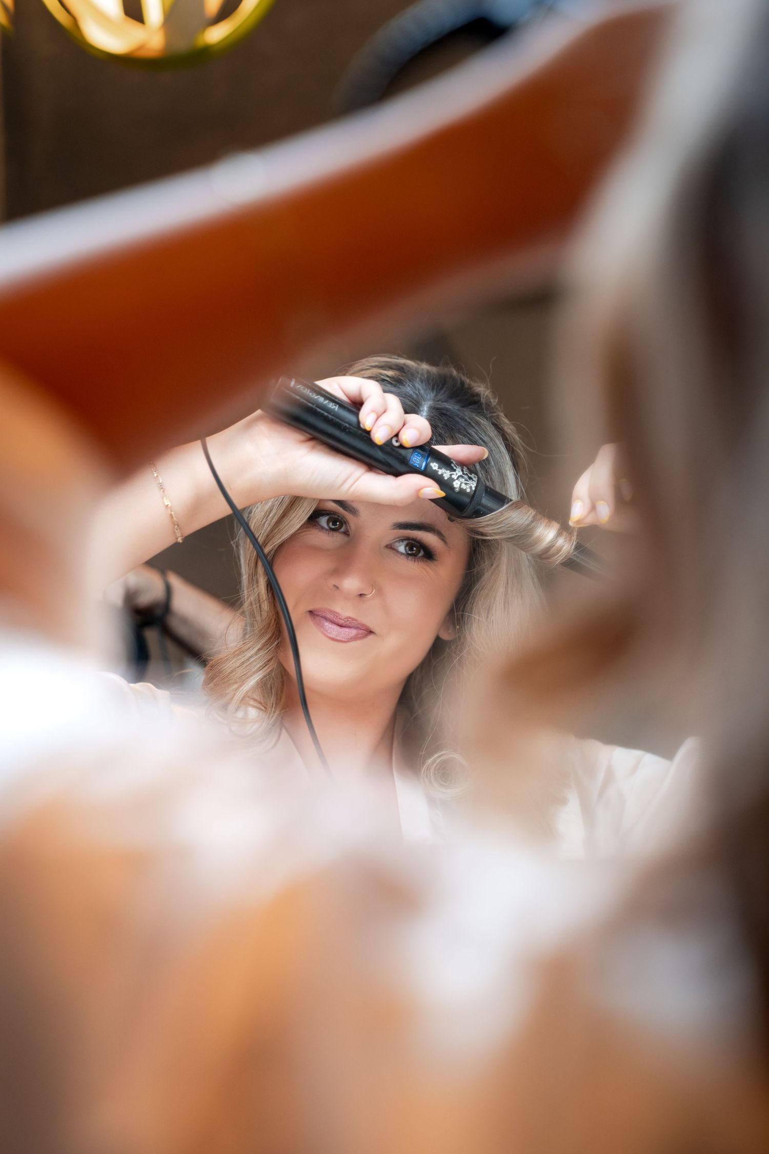 A smiling woman getting her hair styled with a flat iron by a professional hairstylist in a salon setting.