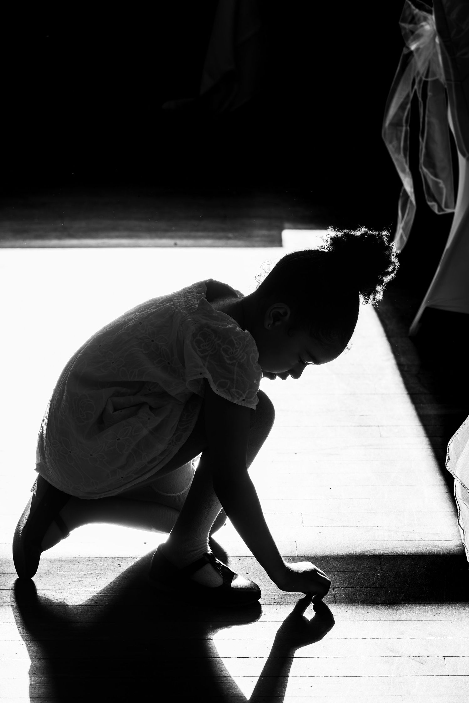 Black and white silhouette of a young child kneeling on a wooden floor in soft backlight.