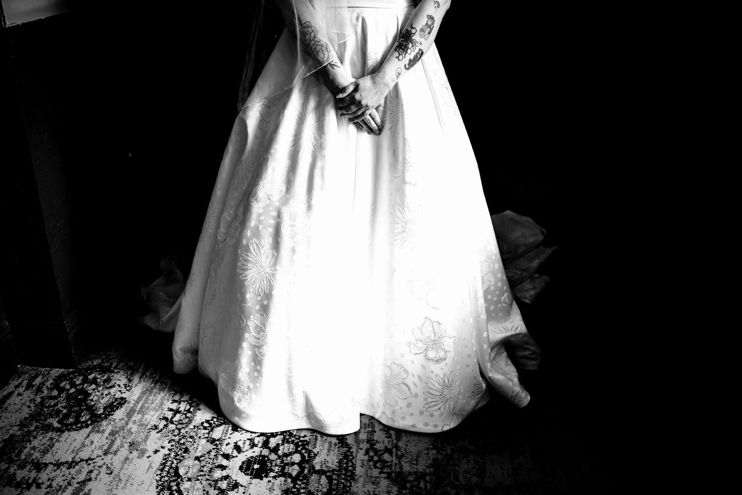 Black and white photo of a bride in a white wedding gown standing on a patterned floor.