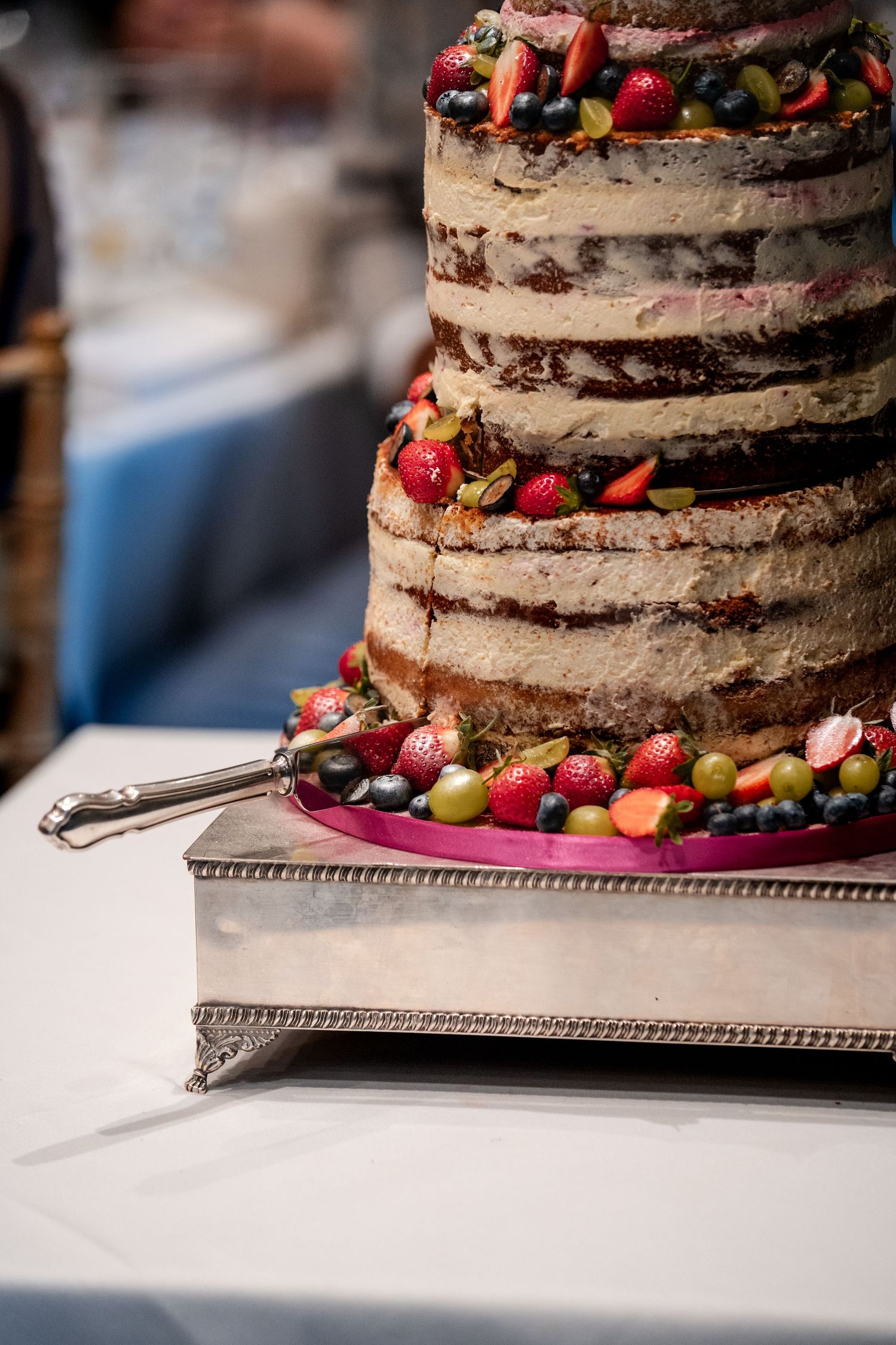Elegant multi-tiered naked wedding cake decorated with fresh strawberries, grapes, and berries on a silver tray.